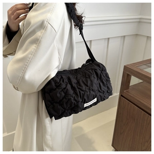 Detail of black quilted shoulder bag with bubble texture and fashion label worn by model