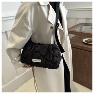 Black quilted tote bag with adjustable shoulder strap worn with a beige trench coat