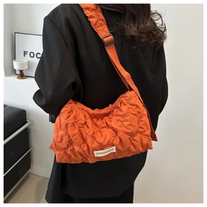 Detail of orange quilted crossbody bag with white fashion tag worn over black blazer