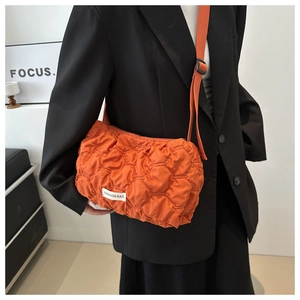 Detail of orange quilted crossbody puff bag with adjustable strap worn on black blazer