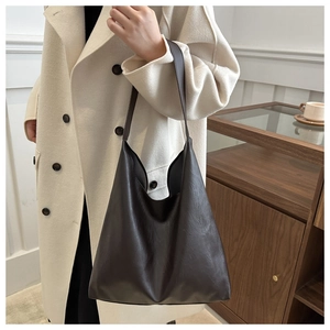 Detailed view of a dark brown large leather tote bag worn by a model in a minimalist room