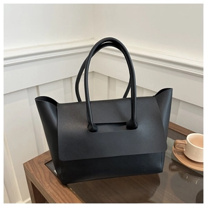 Detail of a black matte leather tote bag with unique flap-through handle on a glass table