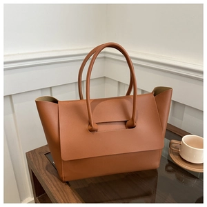 Macro detail of brown leather tote bag with handle through flap on wooden table