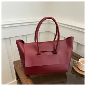 Detail of burgundy leather tote bag with long cylindrical handles on a wooden table