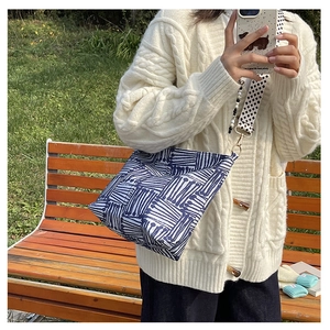 Detailed view of the blue geometric canvas tote bag with a wide checkered strap on a park bench