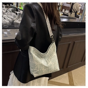 Close-up of canvas tote bag featuring green abstract lines and checkerboard strap detail