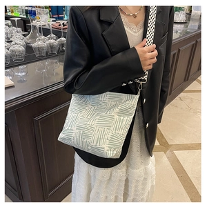 Large canvas tote bag with green stripes and checkered strap worn by a model in a cafe