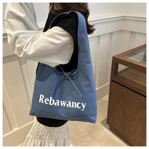 Blue canvas tote bag detail featuring white letter print and decorative side ribbon bow