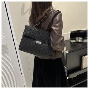 Model wearing large black quilted chain bag with silver twist lock in office setting