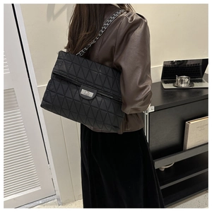 Detail of a large black quilted tote bag with silver chain strap and metal twist lock