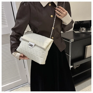 Detail of white quilted crossbody bag with metal chain strap and turn-lock on a model