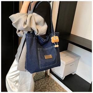 Detail of blue denim tote bag with leather logo patch and cute plush doll charm