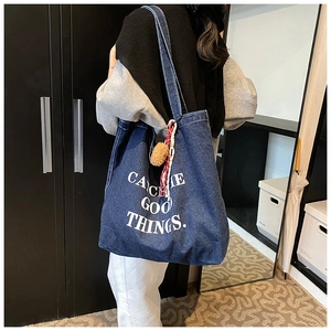 Detail of blue denim tote bag with white text print and plush charms on shoulder strap