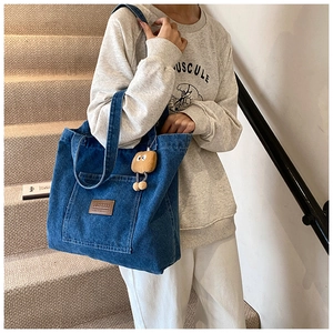 Detail of dark blue denim tote bag featuring brown leather patch and plush charm