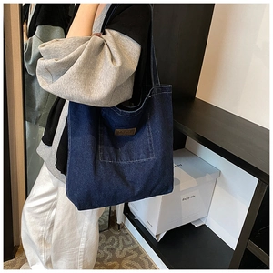 Detail of dark blue denim tote bag featuring external pocket and brown leather tag