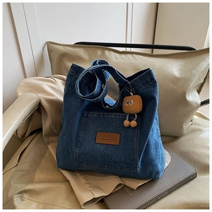 Detail of blue denim tote bag with leather logo patch and cute brown plush charm on a chair