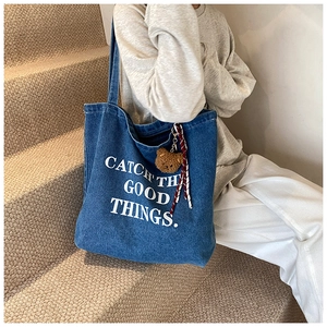 Detail of dark blue denim tote with white letter print and a cute brown bear charm