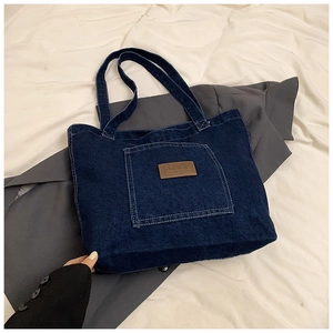 Detail of blue denim tote bag with leather logo patch on textured white fabric