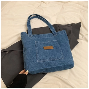 Close-up of blue denim tote bag with leather patch detail and spacious front pocket