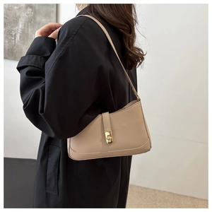 Detailed view of beige underarm bag with gold metal twist lock on black coat