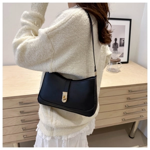 Close-up of minimalist black leather underarm bag with gold hardware buckle and slim strap