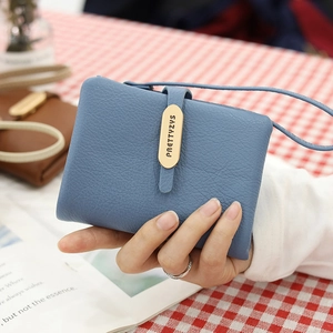 Detail of blue pebble grain leather wallet with gold logo plate and wristlet strap