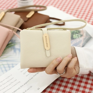 Close-up of minimalist cream PU leather wallet with wristlet strap and golden metal emblem