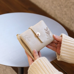 Detail of a beige leather wallet with leaf embroidery and floral hollow metal clasp
