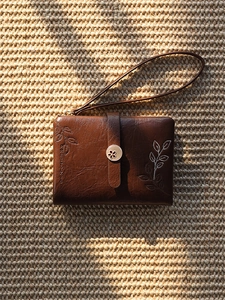 Macro detail of brown leather mini wristlet with leaf embroidery and metal clasp