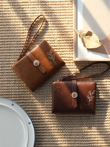 Detail of vintage brown leather wristlet wallet featuring leaf embroidery and flower clasp