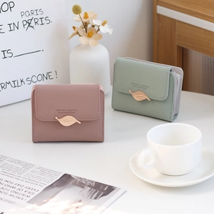 Detail of compact PU leather wallets with leaf clasp and gold brand logo in soft lighting