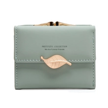 Detail of mint green short wallet featuring gold leaf clasp and engraved slogan text