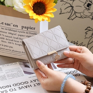 Gros plan d'un petit portefeuille gris matelassé avec pendentif feuille tenu à la main