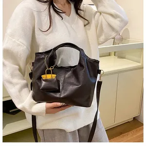 Detail of black faux leather tote bag with gold chain and yellow mini bag charm accessory