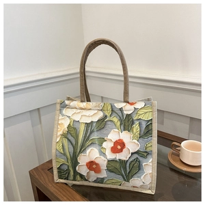 Detail of red and white floral embroidery on a linen tote bag with brown woven handles