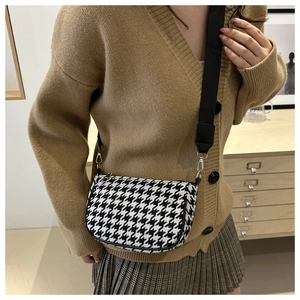 Detail of houndstooth crossbody bag with wide strap and gold hardware on model