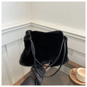 Detail of soft black faux fur shoulder bag with slender leather strap on a table