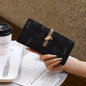 Detailed view of women's long black wallet featuring leaf patterns and gold charms