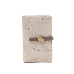 Détail du motif feuille imprimé et du pendentif feuille dorée sur portefeuille beige