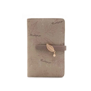 Détail du portefeuille taupe à motif feuilles avec lanière brune et pendentif feuille
