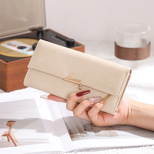 Close-up of cream leather long wallet featuring gold metal logo and delicate heart pendant