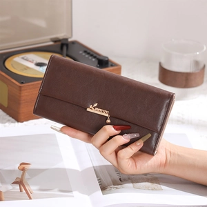 Deep brown long leather wallet featuring a gold leaf pendant held in a lifestyle setting