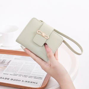 Close-up of light green lychee leather wallet with a bow buckle and hand strap