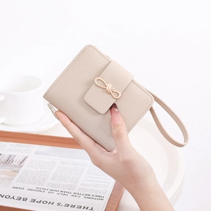 Close-up of beige pebble grain leather wallet with a gold bow buckle and wrist strap