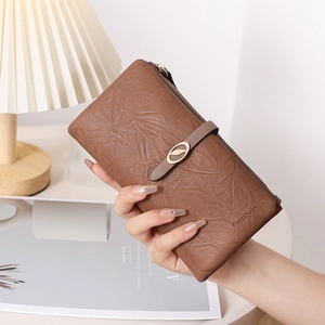 Détail du long portefeuille en cuir marron avec texture de feuilles et pendentif en métal
