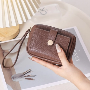 Gros plan sur la texture cuir litchi marron et le bouton pression doré de la pochette