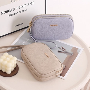 Detailed view of dual zipper lychee leather clutches in lavender and beige with wrist straps
