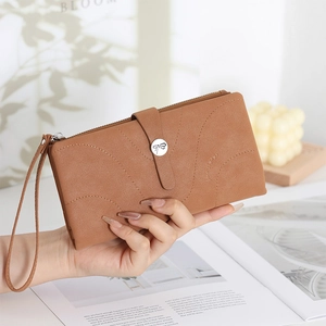 Detail of tan long wallet with stitched pattern, logo buckle, and wrist strap on a magazine