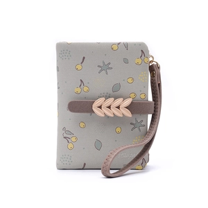 Détail du portefeuille floral avec boucle feuille dorée et dragonne sur tissu bleu clair