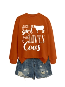 Flat lay of an orange sweatshirt with cow graphic and distressed denim shorts